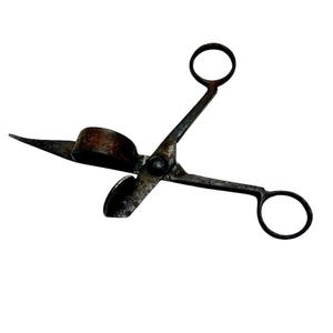 Puede incluir: Tijeras antiguas para apagar velas hechas de metal oscuro. Las tijeras tienen una cuchilla curva y un soporte en forma de copa para extinguir las velas sin humo. Las asas tienen bucles para los dedos.