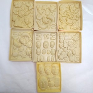 May include: A collection of off-white plastic molds in rectangular boxes. The molds feature various shapes, including sea creatures, faces, and abstract designs. The molds are likely for creating decorative items or crafts.
