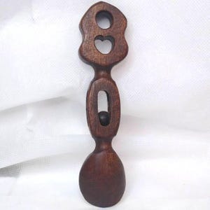 May include: A handcrafted wooden spoon with a dark brown finish. The handle features a heart-shaped cutout and a circular opening. The spoon's bowl is oval-shaped. The spoon is approximately 8 inches long.