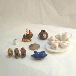 May include: A collection of miniature figurines and accessories. Includes a Santa Claus in a sleigh, a small tea set with floral accents, a blue dish, a coin, a brown vase with a skull design, a small white mug, and three carved monkey figurines.