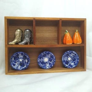 May include: A wooden shelf unit displaying decorative items. It features miniature gold and silver cowboy boots, two orange pumpkin-shaped salt and pepper shakers, and three blue and white patterned dishes.