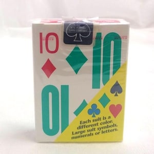 以下が含まれることがあります： 赤とティール色の数字「10」が特徴の、未開封のトランプ。ダイヤ、スペード、クローバー、ハートのマークが含まれています。パッケージには「各スートは異なる色です。大きなスートシンボル、数字または文字」と書かれています。