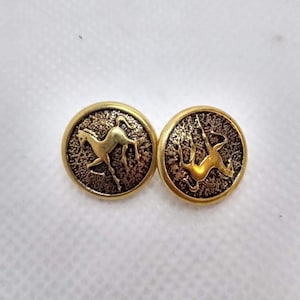 Könnte beinhalten: Zwei goldfarbene Vintage-Knöpfe. Jeder Knopf zeigt ein detailliertes Relief eines Tieres, eines Pferdes und einer Gazelle, vor einem strukturierten Hintergrund. Die Knöpfe sind rund und haben ein klassisches Design.