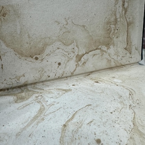 Puede incluir: Primer plano de papel texturizado blanquecino con veteado y motas marrones. El papel est&aacute; parcialmente enrollado, revelando el patr&oacute;n. El dise&ntilde;o se asemeja a la piedra natural o a un efecto acuarela, adecuado para papeler&iacute;a o proyectos art&iacute;sticos.