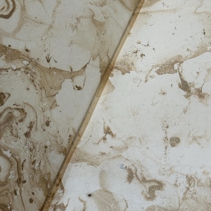 May include: Abstract artwork featuring a marbled design in shades of cream and brown. The pattern has a fluid, organic appearance with swirling textures and subtle color variations. The artwork is divided by a thin, light-colored line.