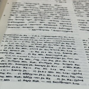 May include: Close-up of a book page with small, densely packed text in black ink. The page is slightly yellowed, suggesting age. The text appears to be in a foreign language, with numerous symbols and abbreviations.