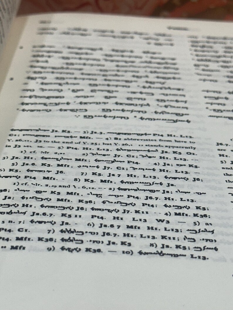 May include: Close-up of a book page with small, densely packed text in black ink. The page is slightly yellowed, suggesting age. The text appears to be in a foreign language, with numerous symbols and abbreviations.