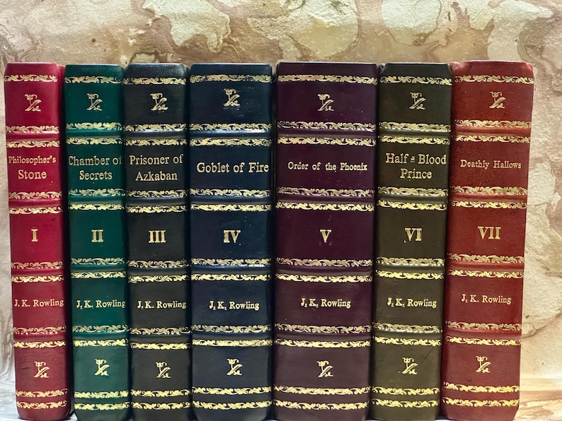 May include: A set of seven hardback books, featuring titles such as "Philosopher's Stone" and "Deathly Hallows." The spines are in shades of red, green, and navy, with gold lettering and decorative details. Each spine displays the author's name, J.K. Rowling.