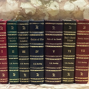 May include: A set of seven hardback books with gold lettering and decorative gold trim. Titles include "Philosopher's Stone," "Chamber of Secrets," and "Goblet of Fire." Each book is a different colour, including red, green, and navy.