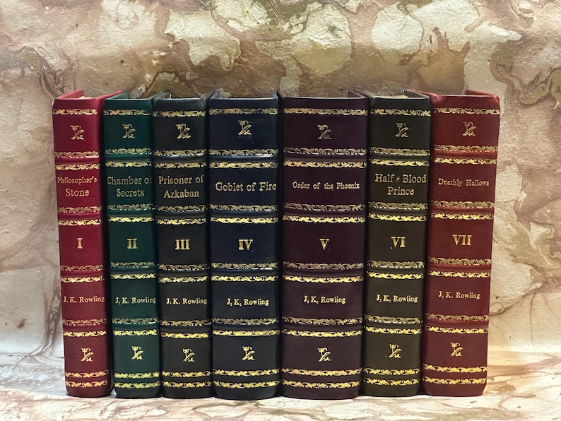 May include: A set of seven hardback books with gold lettering and decorative gold trim. Titles include "Philosopher's Stone," "Chamber of Secrets," and "Goblet of Fire." Each book is a different colour, including red, green, and navy.