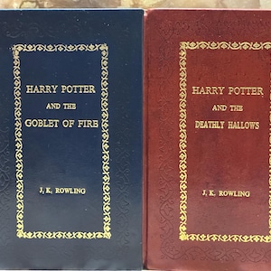 May include: Two hardback books from the Harry Potter series. The first book is dark blue with gold lettering and the title "Harry Potter and the Goblet of Fire" by J.K. Rowling. The second book is burgundy with gold lettering and the title "Harry Potter and the Deathly Hallows".