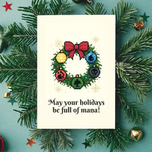 May include: A holiday greeting card featuring a pixelated wreath with colorful ornaments and a red bow. The card is surrounded by evergreen branches and festive decorations. The text on the card reads, "May your holidays be full of mana!"