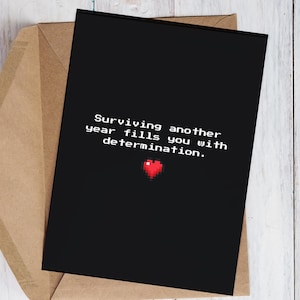 Könnte beinhalten: Schwarze Grußkarte mit dem Text "Surviving another year fills you with determination." und einem pixeligen roten Herz. Die Karte befindet sich in einem braunen Umschlag, ideal für eine ermutigende Nachricht.