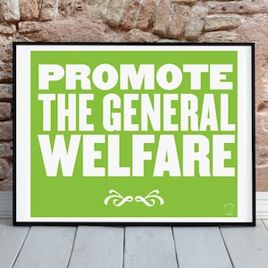 May include: A framed print with the words "PROMOTE THE GENERAL WELFARE" in bold white letters on a bright green background. The print is displayed against a brick wall and white wooden floor.