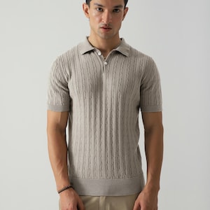 May include: A light brown polo shirt with a textured, vertical cable knit pattern. The short-sleeved shirt has a collared neckline with two buttons. The model is wearing beige trousers.