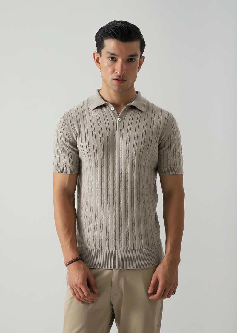 May include: A light brown polo shirt with a textured, vertical cable knit pattern. The short-sleeved shirt has a collared neckline with two buttons. The model is wearing beige trousers.