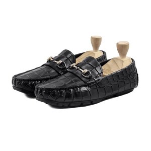 May include: A pair of black leather loafers with a crocodile pattern. Each shoe features a gold-colored metal buckle and is displayed with a wooden shoe tree. The shoes are designed for comfort and style.