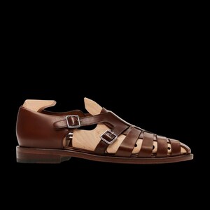 May include: Brown leather sandal with multiple straps and silver buckles. The shoe has a low heel and a wooden shoe form inside. The sandal is designed with a cage-like structure.