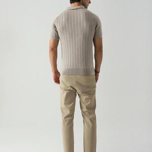 May include: A man wearing a light brown ribbed polo shirt with short sleeves and khaki trousers. The shirt has a collared neckline and a ribbed texture. The trousers are a solid colour and have a straight leg. The man is also wearing brown shoes.