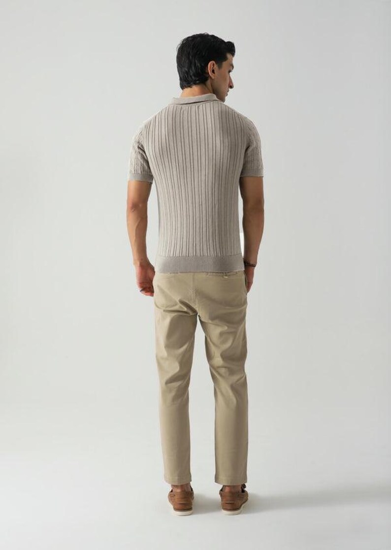May include: A man wearing a light brown ribbed polo shirt with short sleeves and khaki trousers. The shirt has a collared neckline and a ribbed texture. The trousers are a solid colour and have a straight leg. The man is also wearing brown shoes.