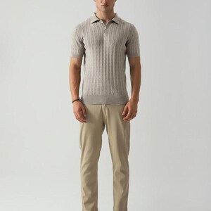 May include: A man in a light brown short-sleeved polo shirt with a textured vertical stripe design, paired with khaki trousers and brown leather boat shoes. The shirt has a zip closure.