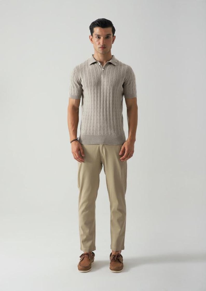 May include: A man in a light brown short-sleeved polo shirt with a textured vertical stripe design, paired with khaki trousers and brown leather boat shoes. The shirt has a zip closure.