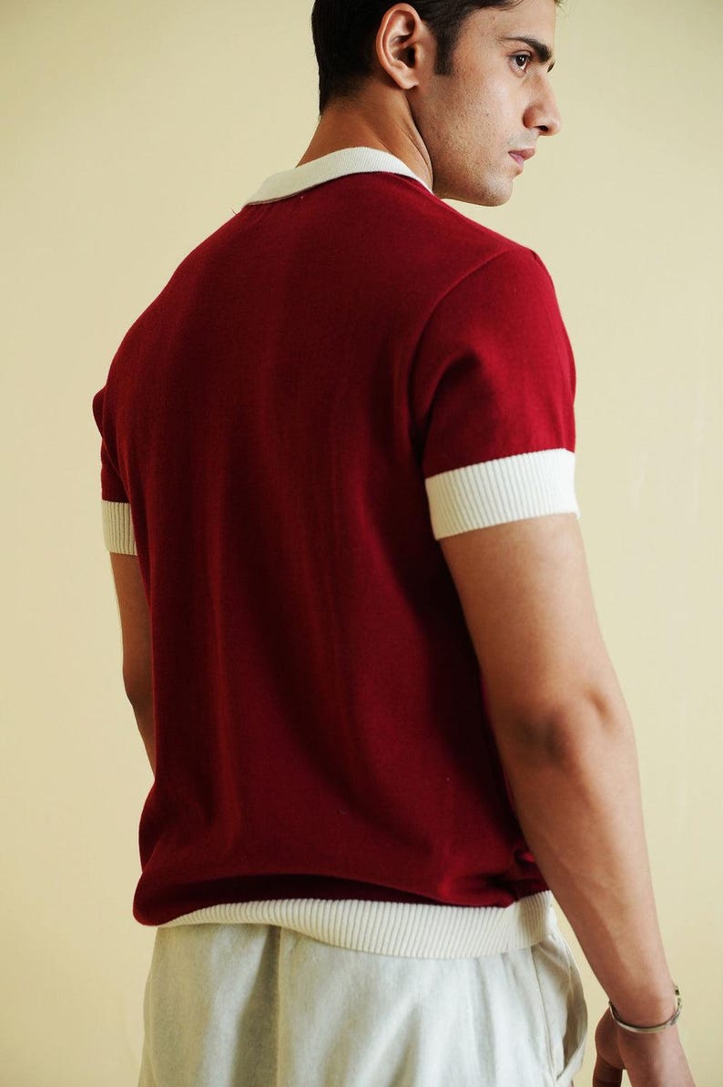 Op de afbeelding: Een bordeauxrood shirt met korte mouwen en witte randen op de kraag en mouwen. Het shirt is gemaakt van een zachte gebreide stof. Het model draagt een lichtgeleurde broek. Het shirt heeft een klassieke, retro stijl.