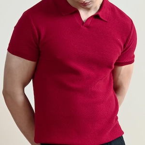 May include: A short-sleeved, red polo shirt with a ribbed texture. The shirt has a classic collar and a v-neck opening. The model is wearing black pants.