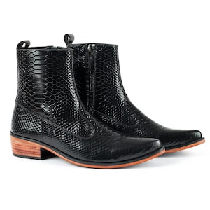 Könnte beinhalten: Schwarze Leder-Ankle Boots mit strukturiertem Schlangenmuster. Die Stiefel haben eine spitze Zehenpartie, einen seitlichen Reißverschluss und einen Holzabsatz. Die Sohle hat einen orangefarbenen Rand.