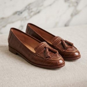 May include: A pair of brown leather loafers featuring a crocodile-embossed texture, a rounded toe, and a decorative tassel detail on the vamp. The shoes have a low heel and a smooth interior lining, showcasing a classic slip-on design.