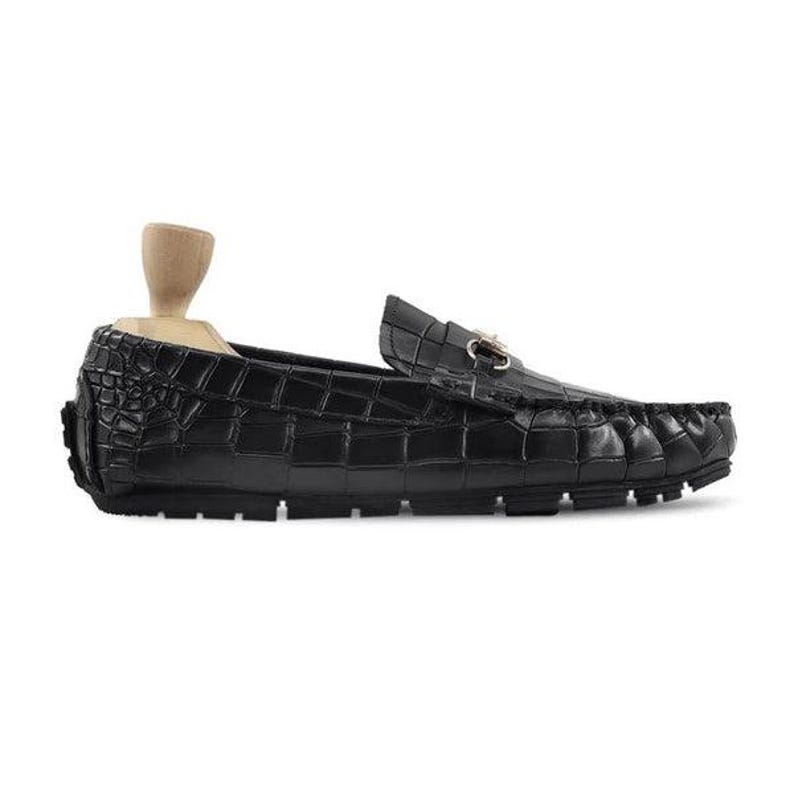May include: Black leather loafer with a crocodile texture. The shoe features a gold-colored buckle and a rubber sole. A wooden shoe form is inside the shoe.