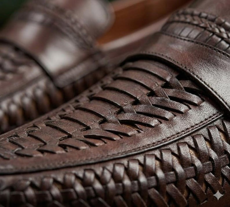 May include: Close-up of brown leather loafers with woven detailing. The shoes have a classic design with a rounded toe and a slip-on style. The leather appears to be high-quality, with a rich, dark brown color and visible texture.