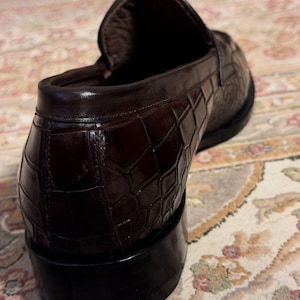 Rear view of a men's burgundy crocodile embossed leather loafer showing the sturdy stacked heel, reinforced heel counter, and detailed scale texture against a patterned rug.