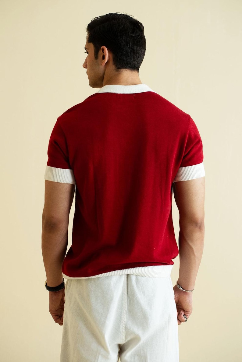 Op de afbeelding: Een rood shirt met korte mouwen en witte details op de kraag en mouwen. De persoon draagt een witte broek. Het shirt is effen van kleur en lijkt van een zacht materiaal te zijn.