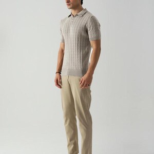 May include: A man in a light brown short-sleeved polo shirt with a ribbed texture, khaki trousers, and brown boat shoes. The shirt has a collar and a partial zip. The outfit is in a neutral colour palette.