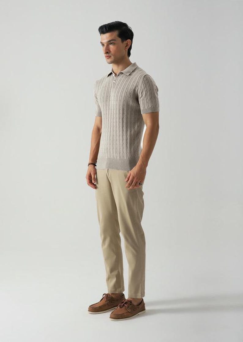 May include: A man in a light brown short-sleeved polo shirt with a ribbed texture, khaki trousers, and brown boat shoes. The shirt has a collar and a partial zip. The outfit is in a neutral colour palette.