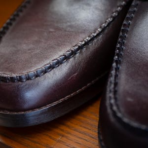 May include: Close-up of a pair of brown leather loafers. The shoes have a classic design with visible stitching around the edges and a smooth, polished surface. The leather appears to be a deep, rich brown color.
