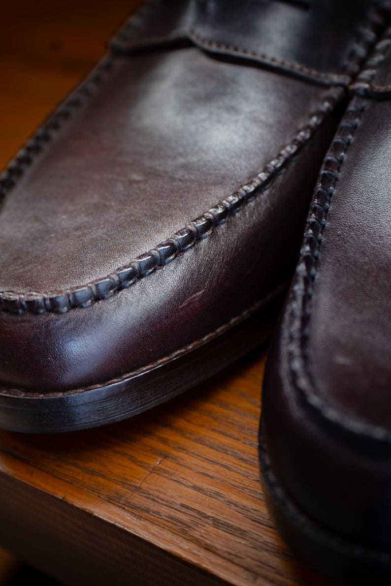 May include: Close-up of a pair of brown leather loafers. The shoes have a classic design with visible stitching around the edges and a smooth, polished surface. The leather appears to be a deep, rich brown color.