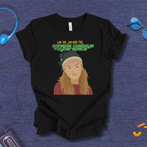 Może przedstawiać: Czarna koszulka z grafiką osoby w kapeluszu i czerwonej koszuli. Tekst "CAN YOU JAM WITH THE CONSOLE COWBOYS in CYBER SPACE" jest wydrukowany nad grafiką w kolorze zielonym i białym.