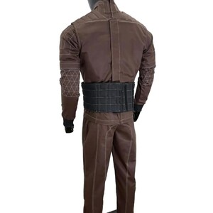 May include: Brown jumpsuit with white stitching and a black belt. The jumpsuit features geometric patterns on the sleeves and a high collar. The mannequin is standing on a black base.