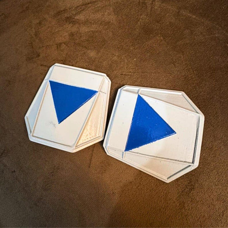 May include: Two white and blue geometric shaped objects with a blue triangle in the center. The objects have a white border and are set against a brown background. The objects are likely decorative.