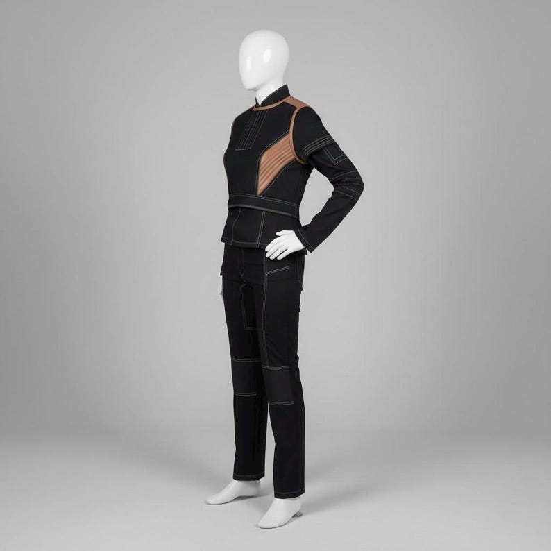 Puede incluir: Un conjunto negro de dos piezas sobre un maniqu&iacute;. La chaqueta tiene detalles en los hombros de color beige y costuras blancas. Los pantalones son negros con costuras blancas en las rodillas y los bolsillos. El conjunto se exhibe en un maniqu&iacute; blanco.