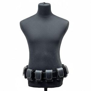 May include: Black leather utility belt with multiple pouches, displayed on a black mannequin. The pouches are rectangular with white stitching. The belt is designed to be worn around the waist.