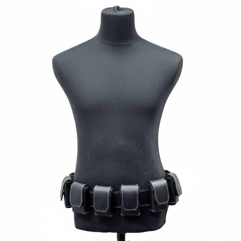 May include: Black leather utility belt with multiple pouches, displayed on a black mannequin. The pouches are rectangular with white stitching. The belt is designed to be worn around the waist.