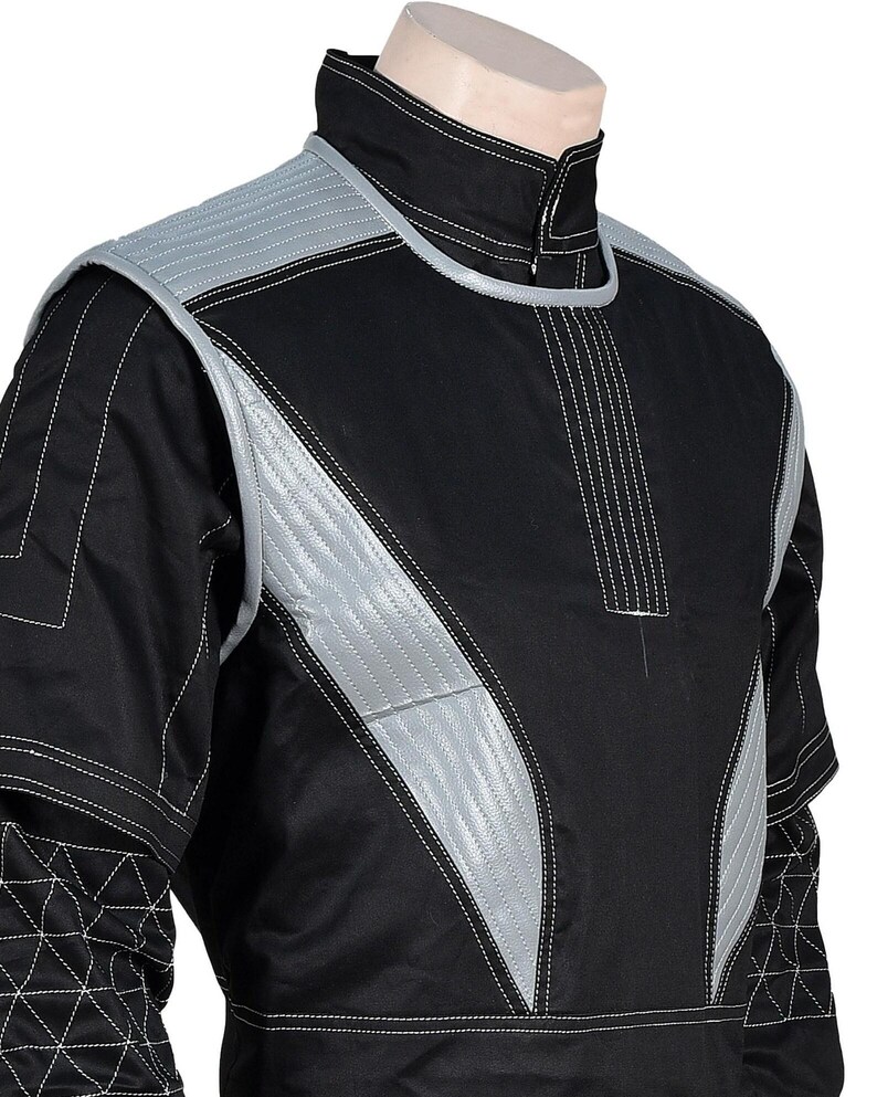 May include: Black jacket with silver accents and white stitching. The jacket features a high collar and quilted silver panels on the shoulders and chest. The design includes geometric patterns and a zipper closure at the neck.