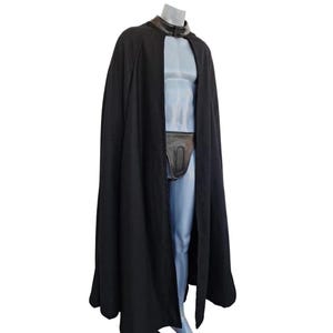 May include: A long, black cape with a leather collar and a matching leather pouch. The cape is draped over a mannequin, showcasing its flowing design. The outfit is a costume.