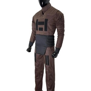 May include: A brown costume with a high collar, long sleeves, and matching pants. The costume features a black panel across the midsection and the letter "H" on the chest. White stitching accents the seams. The costume is displayed on a black mannequin.