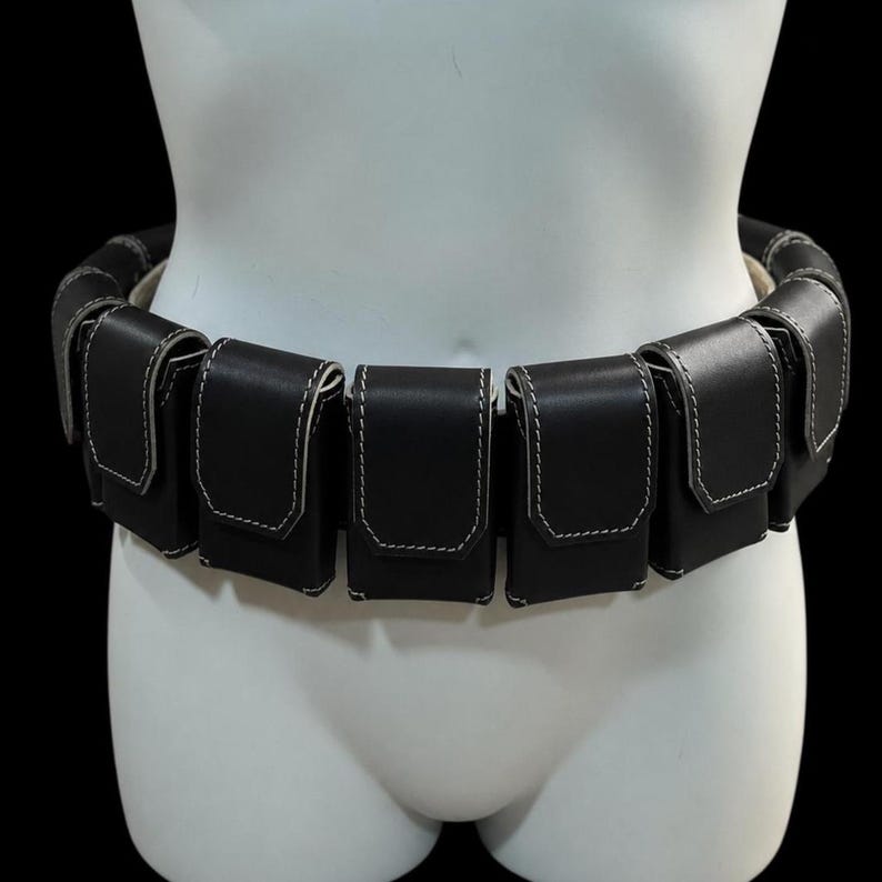 May include: A black leather utility belt with multiple pouches, each outlined with white stitching. The belt is displayed on a white mannequin, showcasing its design and construction. The pouches are evenly spaced around the belt's circumference.
