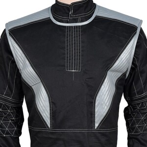 May include: Black racing suit with silver accents on the shoulders and chest. The suit features white stitching details and a high collar. The design includes quilted panels and a front zipper.
