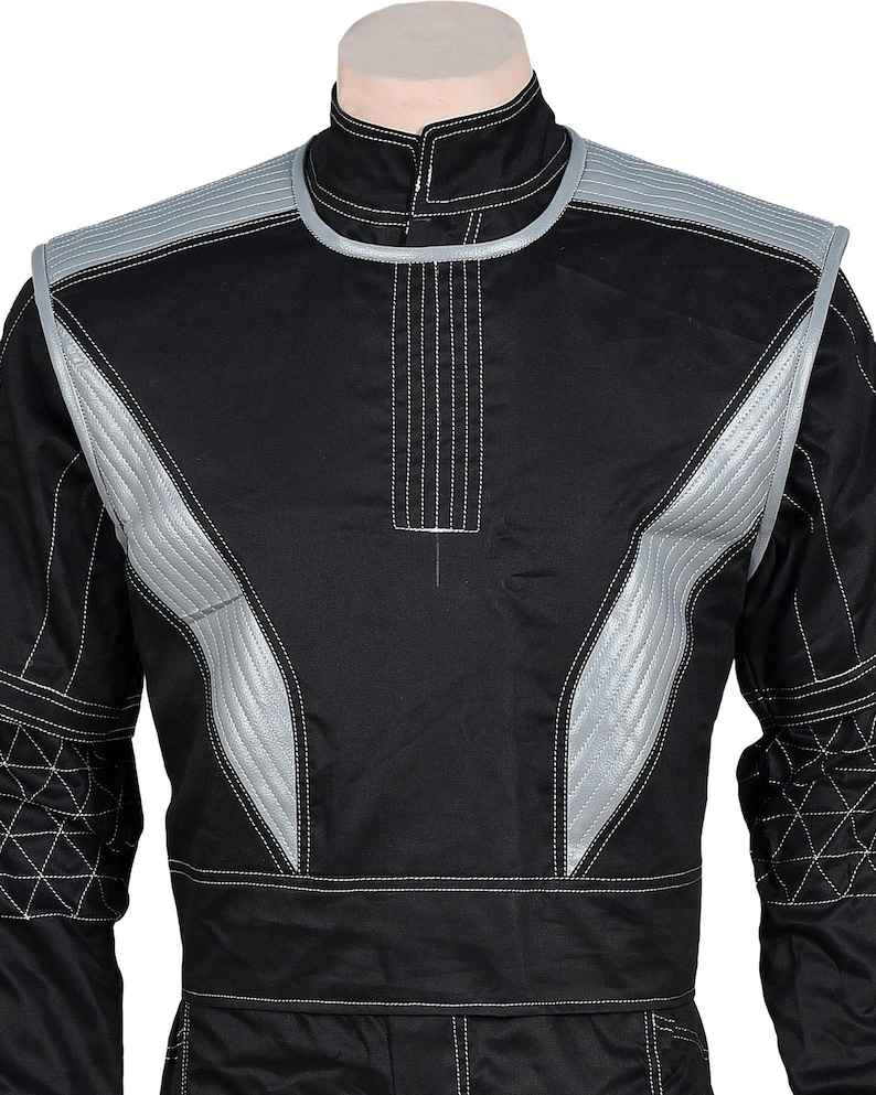 May include: Black racing suit with silver accents on the shoulders and chest. The suit features white stitching details and a high collar. The design includes quilted panels and a front zipper.